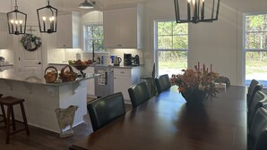 A spacious kitchen with white cabinets, a large island with a sink, and a dining area with a wooden table and chairs. - Cottage near Elijah State Park, Savannah Lakes Village, Baker and Hickory Knob. (Lincolnton)