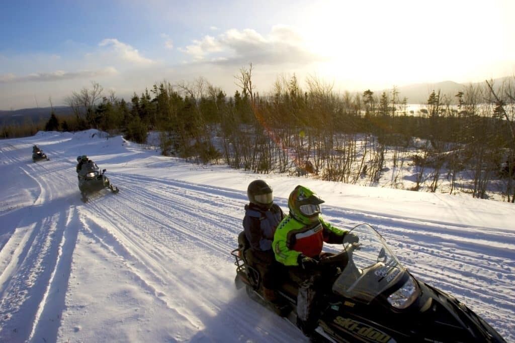 Un sendero para motos de nieve en una zona boscosa con cielo despejado.