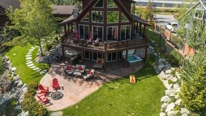 A two-story cabin with a balcony, a hot tub, and a patio area with outdoor furniture. - Waterfront Log Home, Dock, Hot Tub, and Pickleball (Sagle)