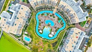 Luftaufnahme eines Resorts mit einem zentralen Pool, mehreren kleineren Pools und einem kreisförmigen Gebäudebau.