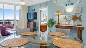 Ein modernes Wohnzimmer mit einem Glastisch, gewobenen Platzsets, einem Deckenventilator und Blick ins Freie.