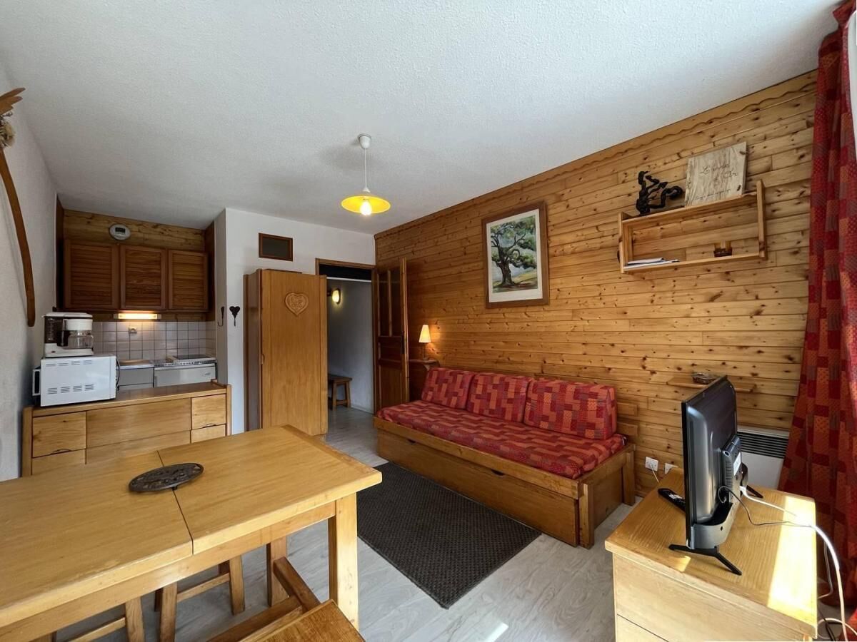 Un espacio habitable compacto con sofá de madera, mesa de comedor, kitchenette y televisor.