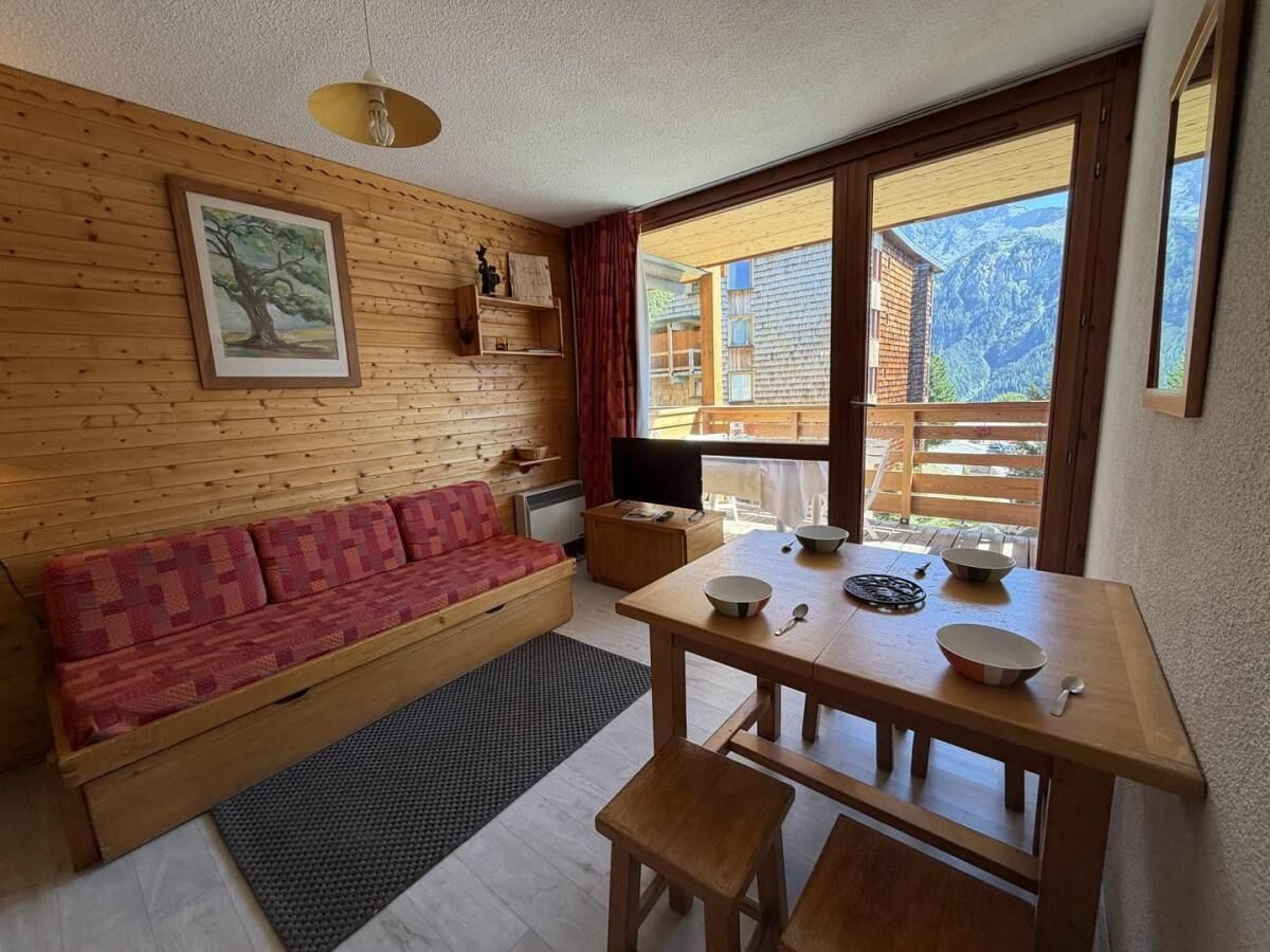 A cozy room with a wooden sofa, a dining table with bowls, and a large window offering a mountain view.
