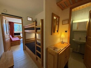 Een kleine kamer met een stapelbed, een bureau, een spiegel en een bedlampje.