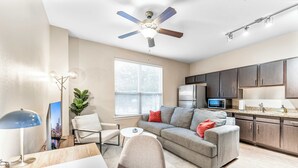 A modern living room with a gray sofa, a dining table, and a ceiling fan.