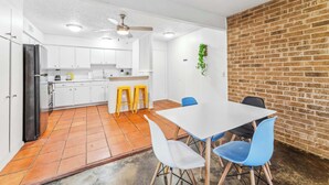 Cocina compacta con armarios blancos, un refrigerador negro y un comedor con mesa blanca y sillas azules.