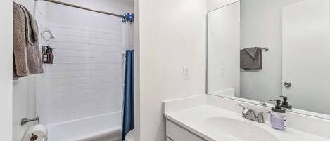 A bathroom with a white bathtub, a sink with a mirror, and a towel rack.