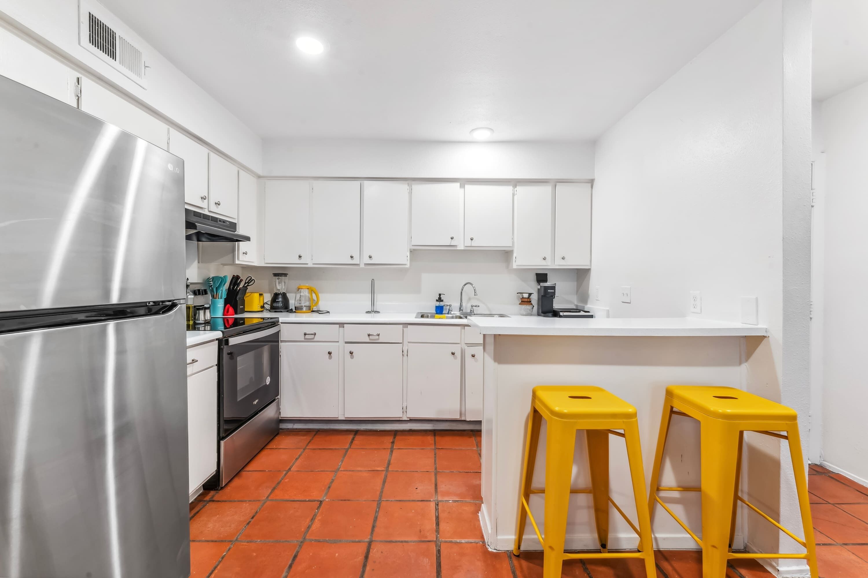 A modern kitchen with white cabinets, a stainless steel refrigerator, and a tiled floor.