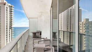 Un balcon doté de meubles en osier, d’une table et de chaises, offrant une vue sur une étendue d’eau et des immeubles de grande hauteur.