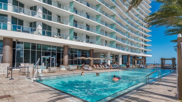 Un espace piscine d’hôtel doté de plusieurs niveaux de balcons, de chaises longues et de parasols.