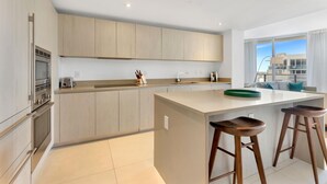 Une cuisine moderne dotée d’un îlot central, d’appareils électroménagers en acier inoxydable et offrant une vue sur la ville.