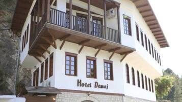 Hotel Demaj features a traditional two-story building with a balcony on the upper floor, a stone archway entrance, and a glass door.