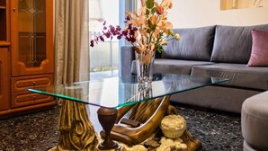 Une table dont le plateau est en verre, avec un socle décoratif en bois, un vase rempli de fleurs et une petite figurine posée sur un comptoir en granit.