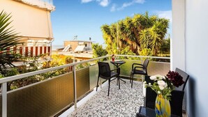 Un balcon avec deux chaises et une table, d’où l’on peut admirer un paysage urbain et des palmiers.