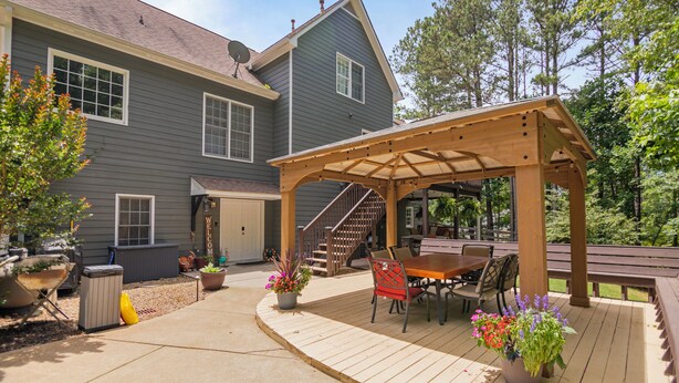 Une maison à deux étages dotée d’un patio couvert agrémenté d’une pergola en bois, de meubles d’extérieur et de plantes en pot.