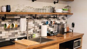 Une cuisine avec un plan de travail en bois, un évier, une machine à café et un panneau au-dessus de l’étagère.