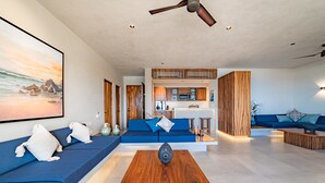 A modern living room with a blue sofa, a wooden coffee table, and a kitchen in the background. - Private Oceanview Splash Pool & Beach Access (Huatulco)