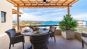 A covered outdoor dining area with wicker chairs, a table set with a bowl of fruit, and a view of the ocean. - Private Oceanview Splash Pool & Beach Access (Huatulco)