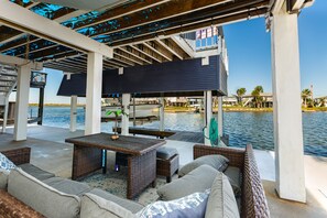 Un patio al aire libre con mobiliario de mimbre, una mesa y vista al agua.