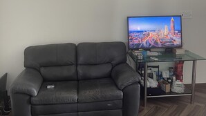 En stue med en sort lædersofa, et glasbord og et fladskærms-tv, der viser et bybillede.