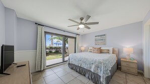 A bedroom with a bed, a ceiling fan, a TV, a nightstand, and a view of the outdoors.