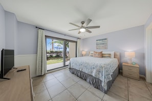 Une chambre à coucher comprenant un lit, un ventilateur de plafond, une télévision, une table de chevet et une vue sur l’extérieur.