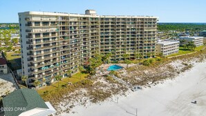 A high-rise hotel with multiple balconies, a swimming pool, and a beach view.