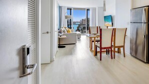 A modern kitchen with a stainless steel refrigerator, a dining area with a table and chairs, and a living room with a sofa and a view of the city. - Stylish 2BR Apt w/Views (Pool & Gym) (Hallandale Beach)