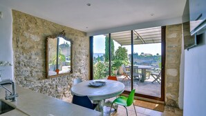 A room with a stone wall, a round table with chairs, a mirror, and a view of the outdoors. - Maison Eclaircie - Three Bedroom Villa, Sleeps 6 (Gordes)