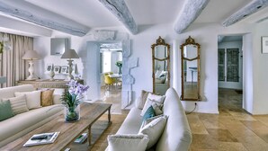 A spacious living room with a high ceiling, exposed beams, and a large mirror. A sofa and coffee table are positioned in the foreground, with a dining area visible in the background. - Maison Eclaircie - Three Bedroom Villa, Sleeps 6 (Gordes)