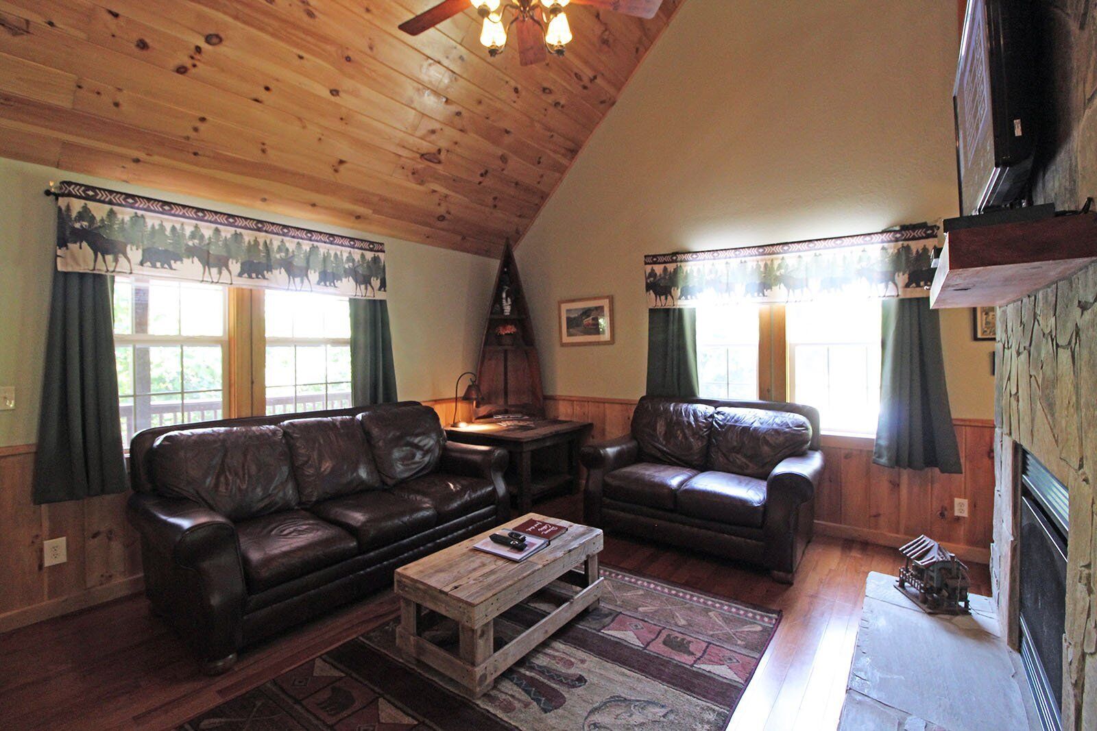A cozy living room with a wooden ceiling, two leather sofas, a coffee table, and a fireplace.