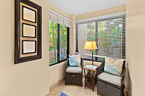 Ein Eckzimmer mit einem Korbstuhl, einem kleinen Tisch mit Lampe und einem Fenster mit Jalousien.