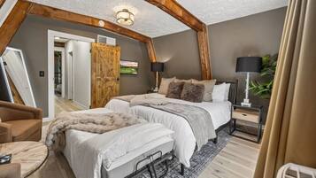 A bedroom with a lofted ceiling, a bed with white bedding, a wooden door, and a nightstand with a lamp.