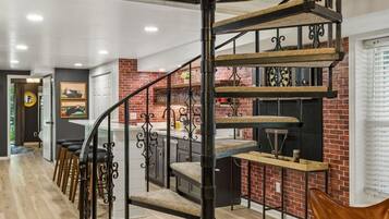 Un escalier en colimaçon à plusieurs niveaux, avec une finition en bois et des rampes en métal, menant à un espace cuisine doté d’un mur en briques et d’appareils électroménagers modernes.