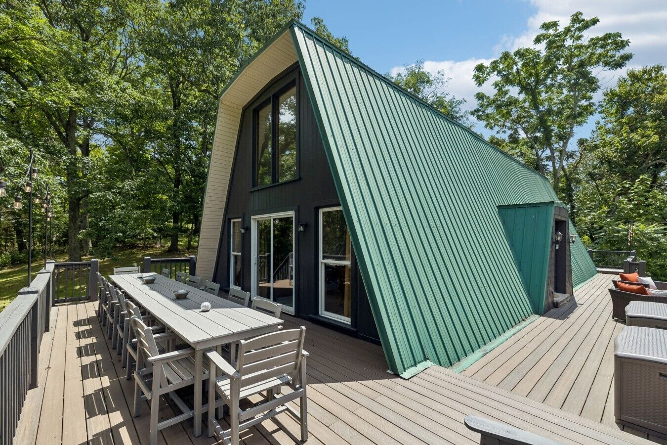 A modern house with a sloped roof, large windows, and a deck with outdoor furniture.