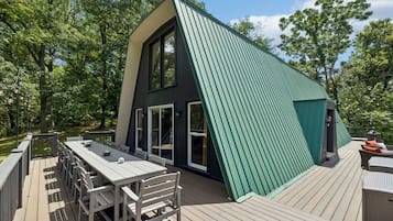 A modern house with a sloped roof, large windows, and a deck with outdoor furniture.
