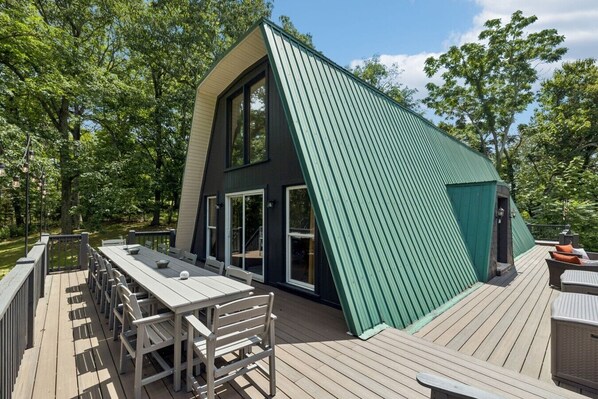 Una casa moderna con techo inclinado, ventanas amplias y una terraza con mobiliario exterior.