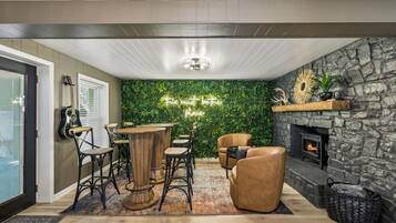 A cozy room with a stone fireplace, a green wall with a neon sign, and a wooden coffee table with chairs.