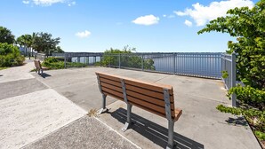 Un banc situé au bord de l’eau, avec une rambarde en métal et de la verdure.