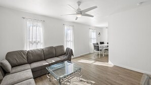 Un salon moderne avec un canapé d’angle gris, une table basse en verre et un ventilateur de plafond.