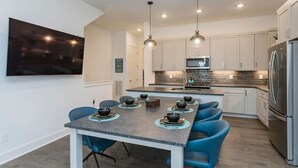 A modern kitchen with a dining area, stainless steel appliances, and blue chairs.
