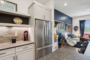 A modern kitchen with a stainless steel refrigerator, a coffee maker, and a clock on the wall.