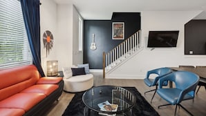 A modern living room with a sofa, chairs, a coffee table, a staircase, and a TV.