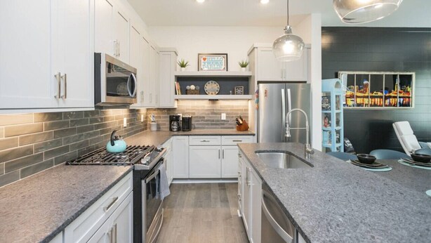 A modern kitchen with white cabinets, a stainless steel refrigerator, a gas stove, and a pendant light.