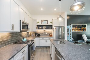 A modern kitchen with white cabinets, a stainless steel refrigerator, a gas stove, and a pendant light.