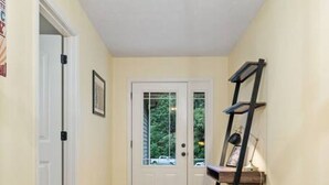 Un couloir avec un plancher en bois, une porte blanche et une échelle noire appuyée contre le mur.