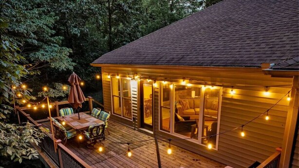 Une terrasse en bois, dotée de mobilier d’extérieur et illuminée de guirlandes lumineuses.