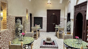 A courtyard with multiple round tables and chairs, a decorative fountain, and a large dark wooden door. - Riad Sakura Marrakech  (Marrakech)
