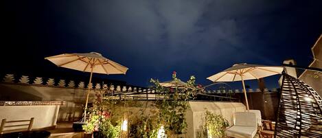 An outdoor patio area with multiple potted plants, wooden chairs, and umbrellas.