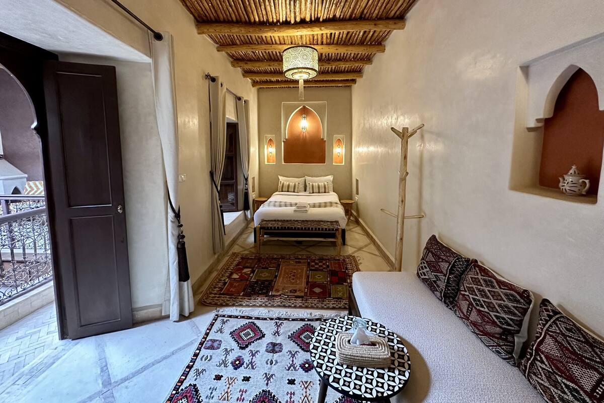 A room with a bed, a sofa, a patterned rug, a wooden ceiling, and a small table with a tissue box.
